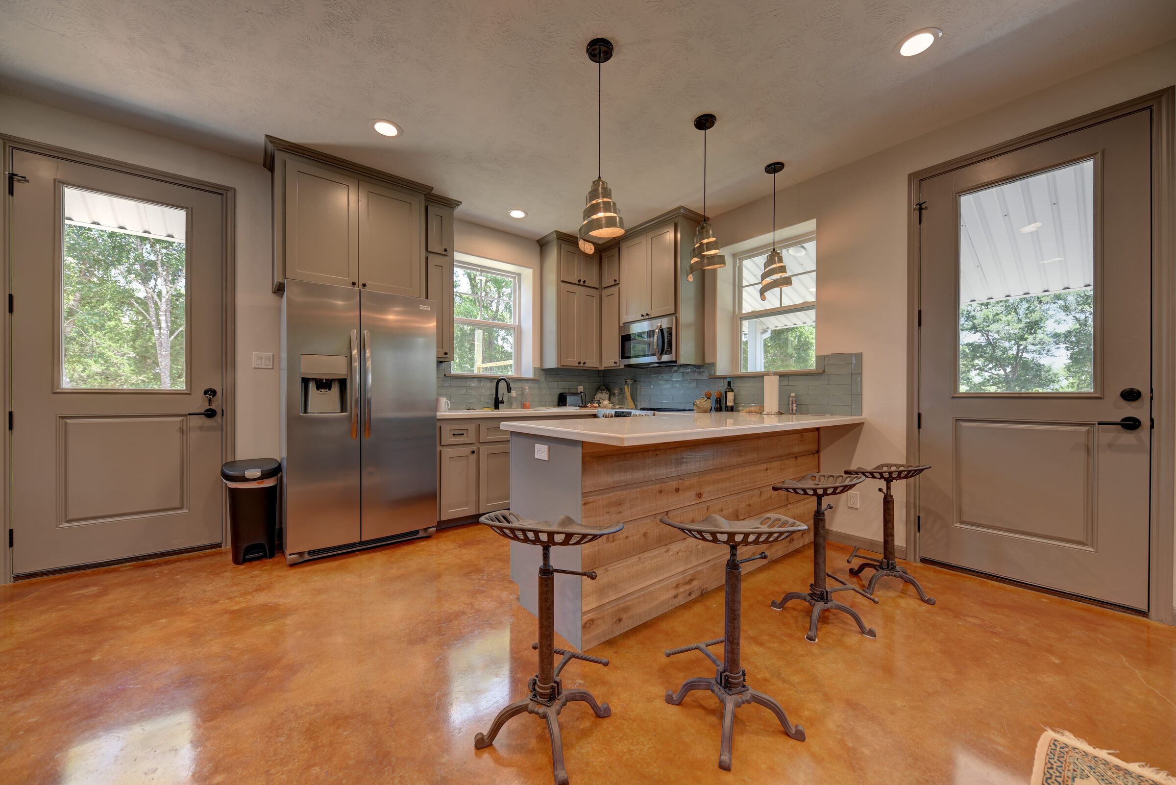 Barndominium kitchen with a stained concrete floor, grey shaker cabinets, a reclaimed-wood island and tractor-seat stools