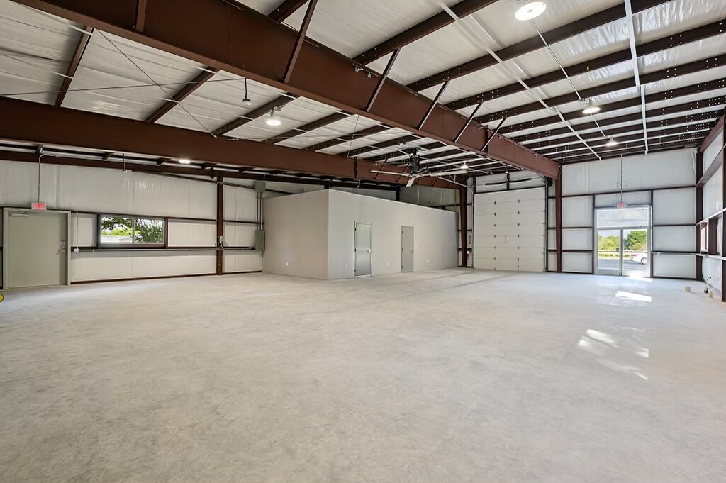 Open warehouse interior with red iron framing, insulated walls and roof, an overhead door and a framed interior office