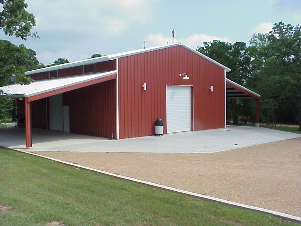 Red 40 by 60 party barn in College Station, Texas with white trim, an overhead door on the end wall and lean-tos on both sides