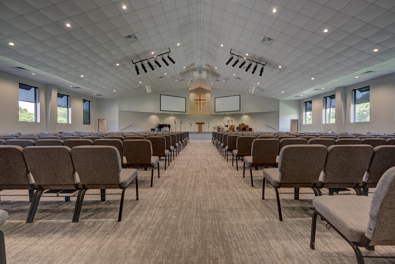 Sanctuary looking toward the platform, with a vaulted acoustic ceiling, a wooden cross and projection screens