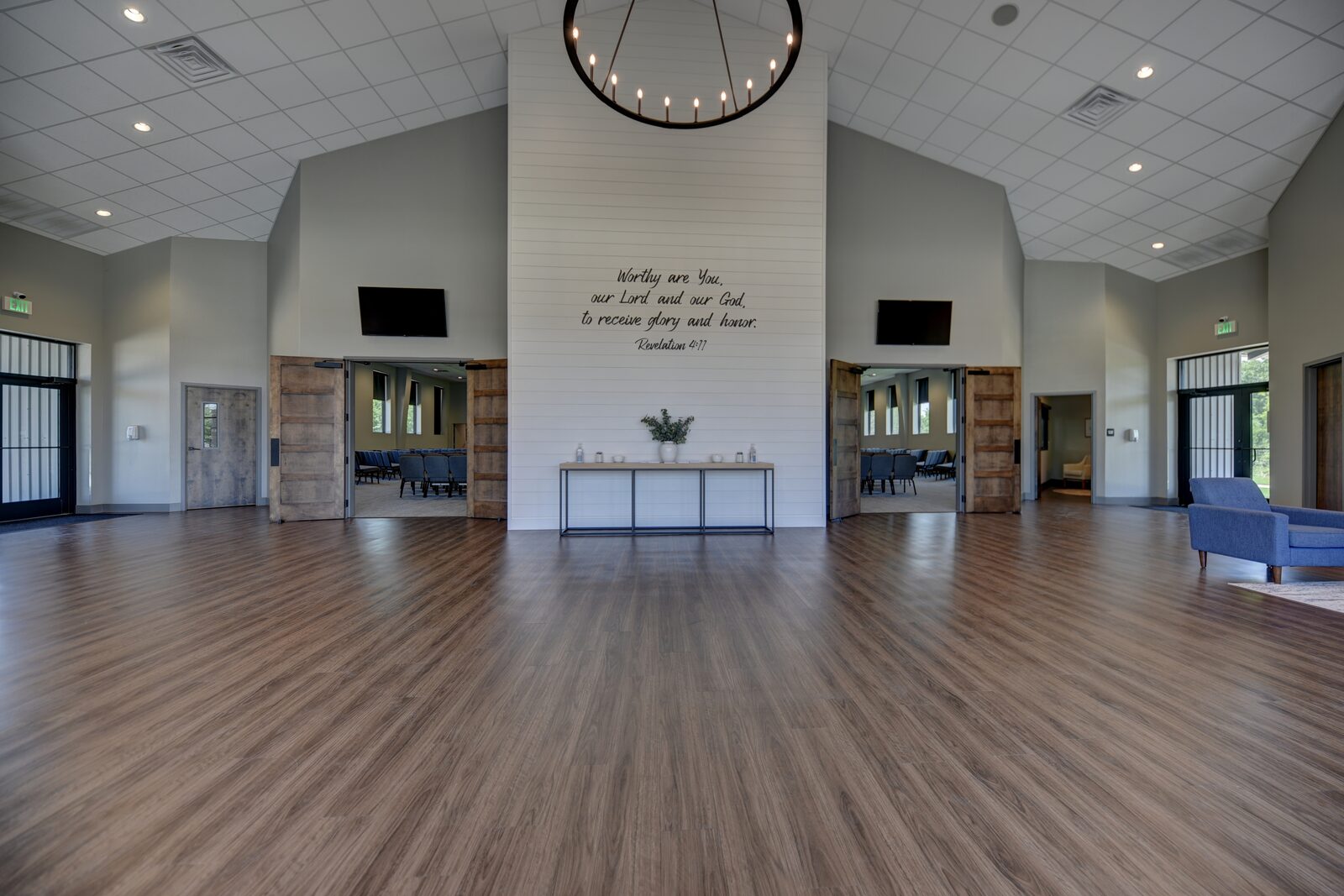 Church foyer with a shiplap scripture wall, chandelier and sliding barn doors opening into the sanctuary