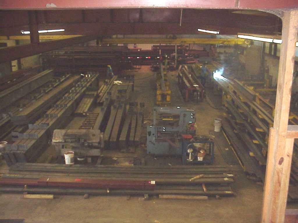 Steel members laid out for fabrication in the Rhodes Building Systems shop, with welding under way at the far end