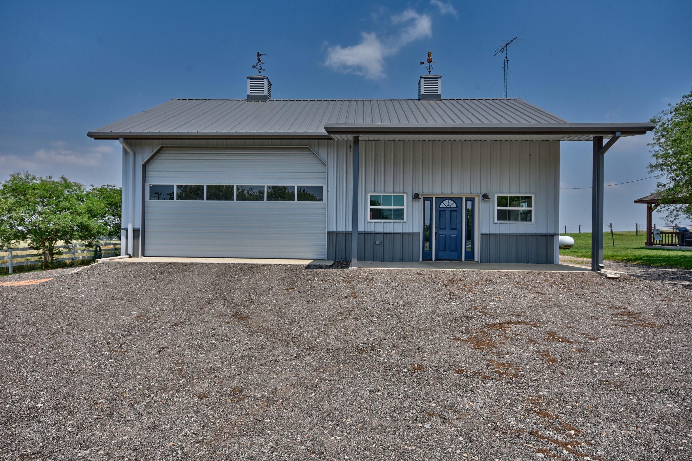 Front elevation of the metal shop building with a wide roll-up door, cupolas and weathervanes on the ridge
