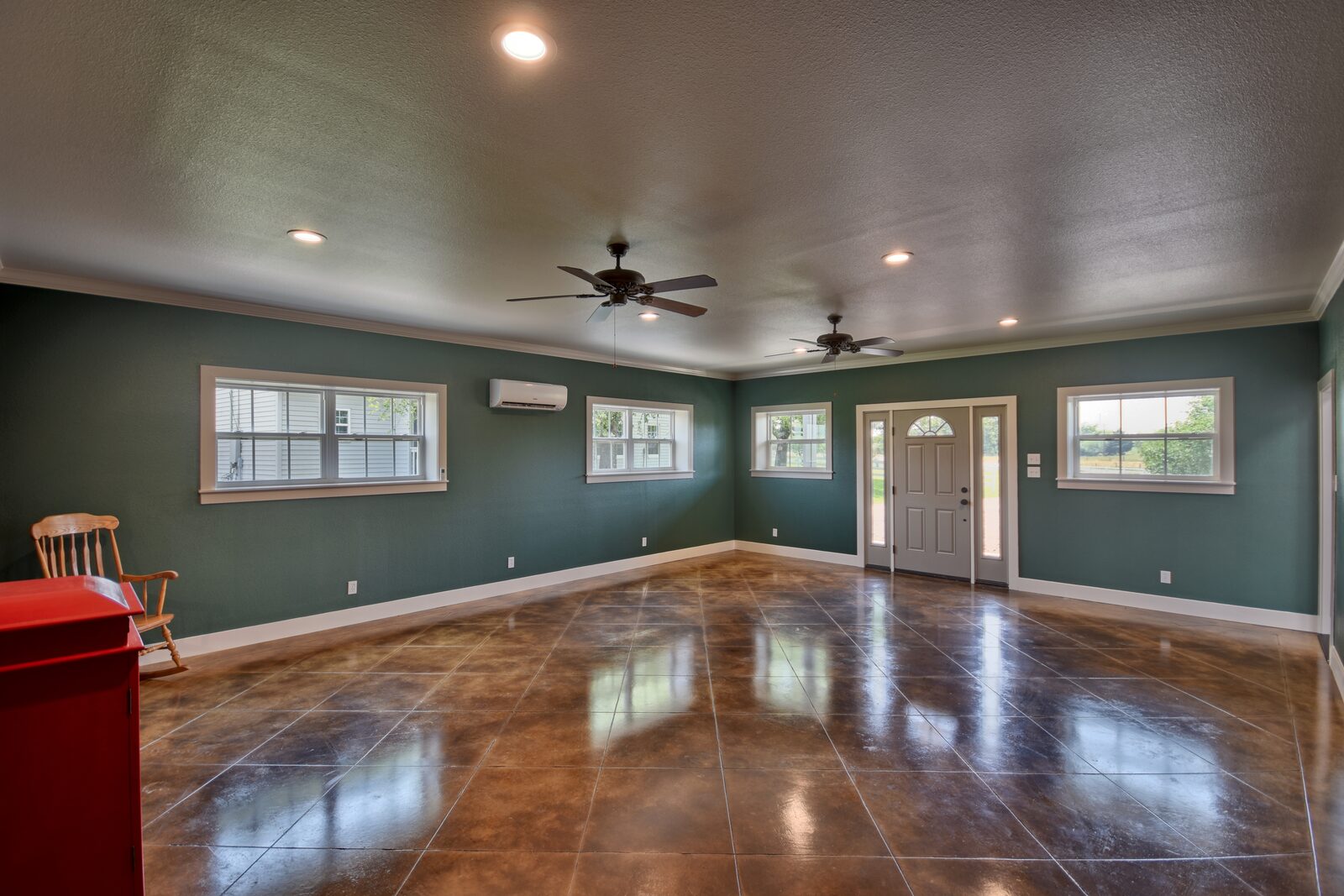 Game room with deep green walls, stained and scored concrete floor and the front entry door