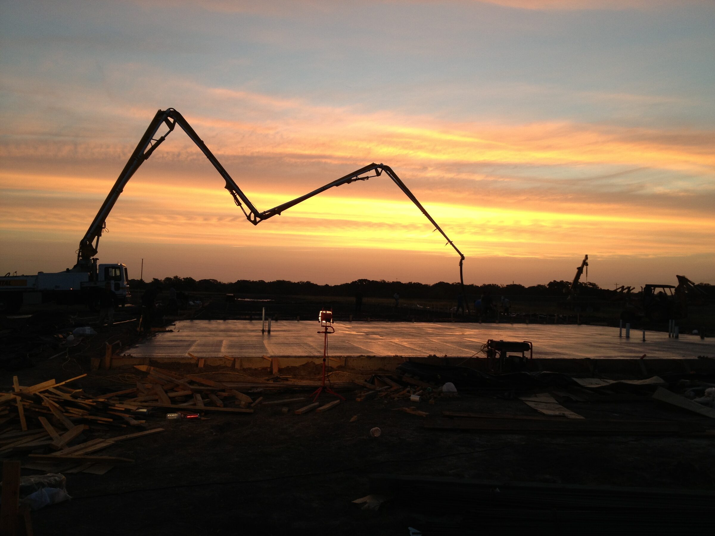 Concrete pump boom silhouetted against a Texas sunset over a freshly poured building slab