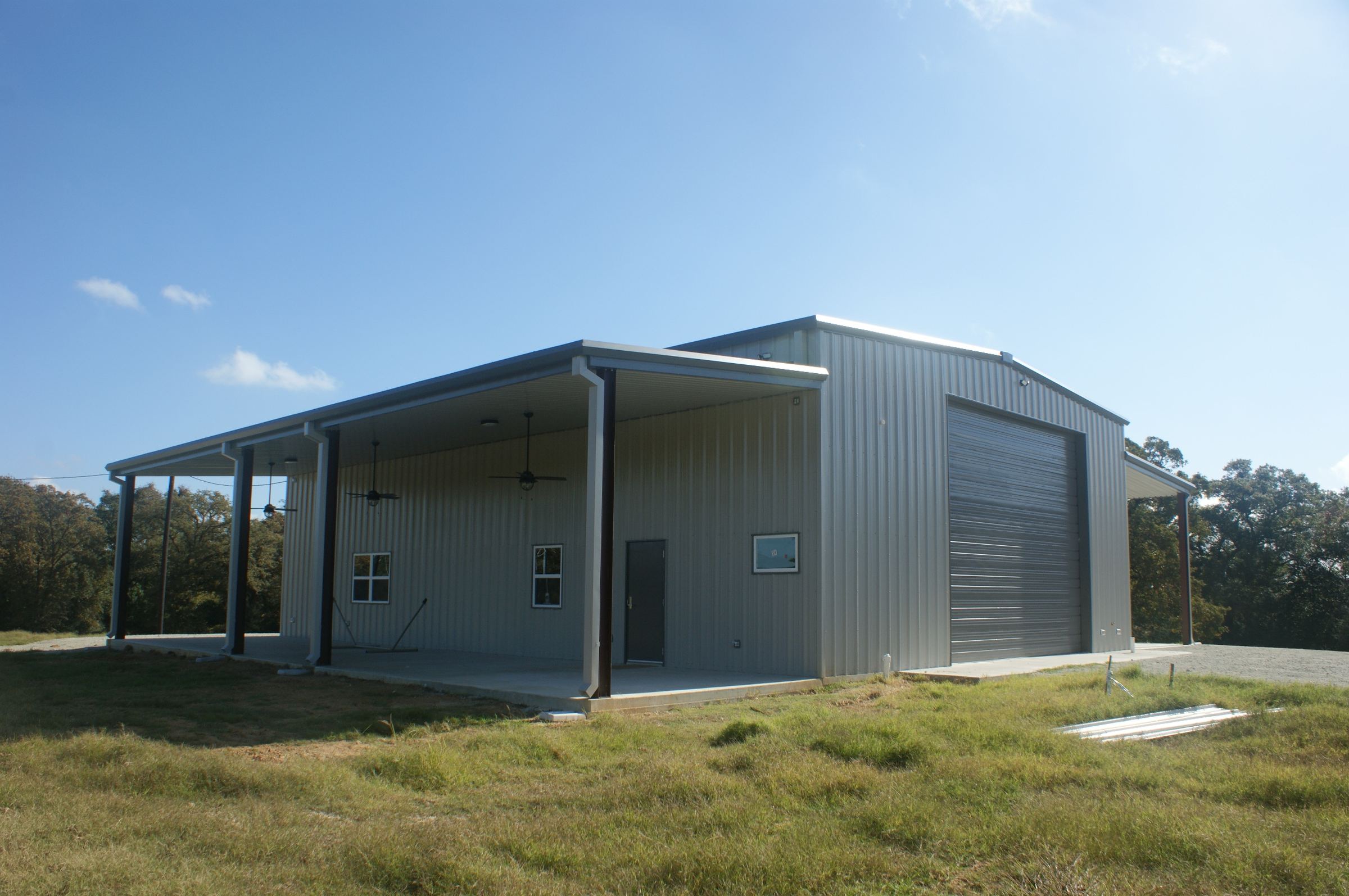 A completed Rhodes Building Systems shop building with lean-tos, a covered porch and oversized roll-up doors