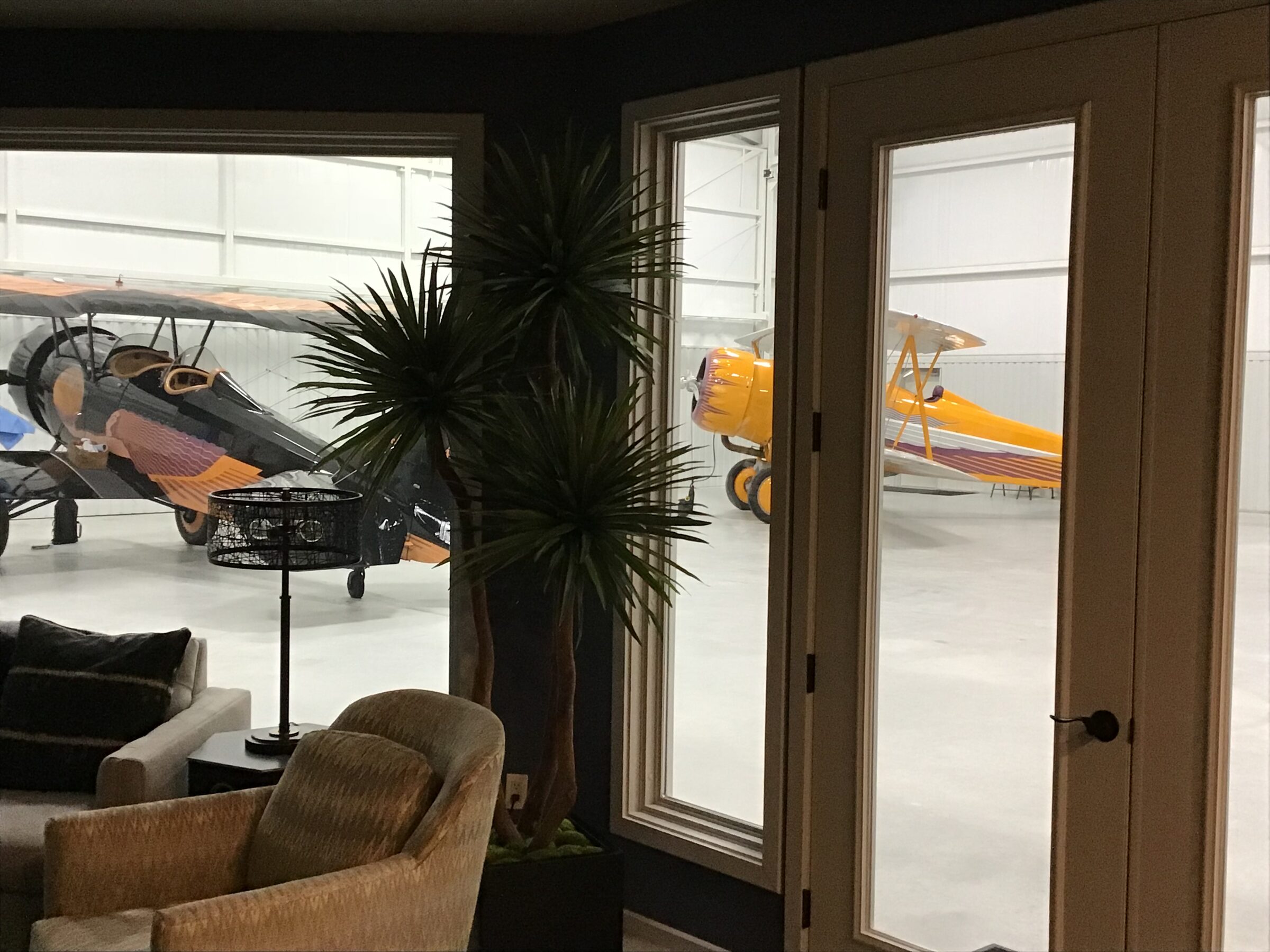 Vintage biplanes parked in a finished hangar, seen through the windows of the attached lounge